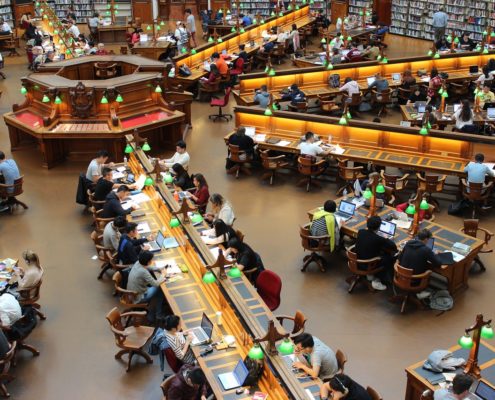 photo d'une grande bibliothèque anglaise avec de longues tables en étoile autour d'un ilot central, des lampes vertes et des étudiants alignés les uns à côtés et en face des autres.... Pour imager la concentration