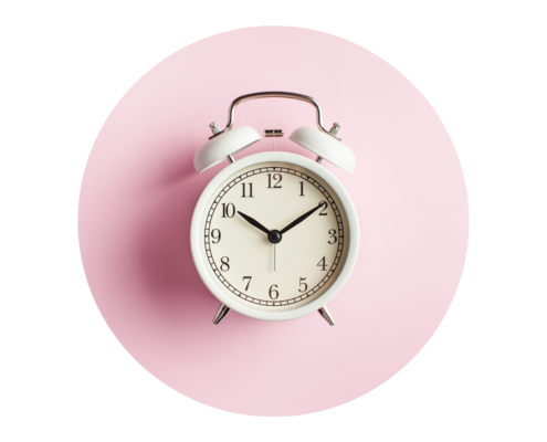 photo d'un réveil mécanique blanc sur fond rose poudré pour illustré la question abordée : "Qu'est-ce que l'heure?"