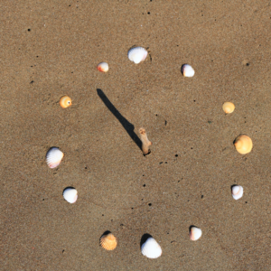 cadran solaire créé dans le sable : au centre un bâton planté droit, et tout autour des coquillages pour représenter les heures. Photo source Canva